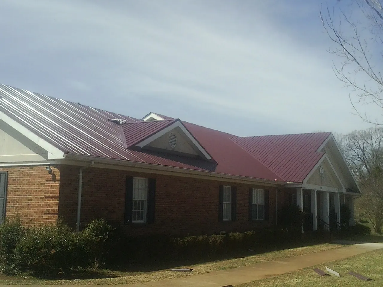 Red metal roof with gabled entries on a long brick building, from a Hail Damage Roof Repair job in Westville