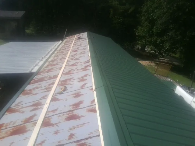 Old rusted panels beside newly installed green metal roofing — Wind Damage Roof Repair by Roofing Brothers in Westville