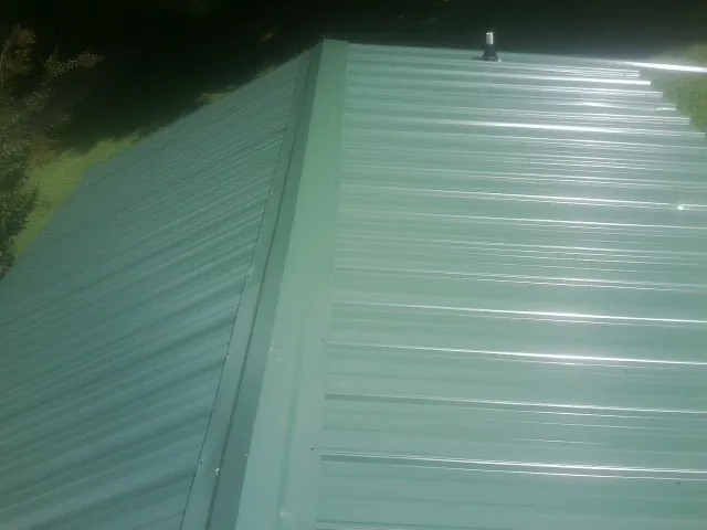 New green metal panels meeting at the ridge of a roof — Flat Roof Repair work by our crew in Westville