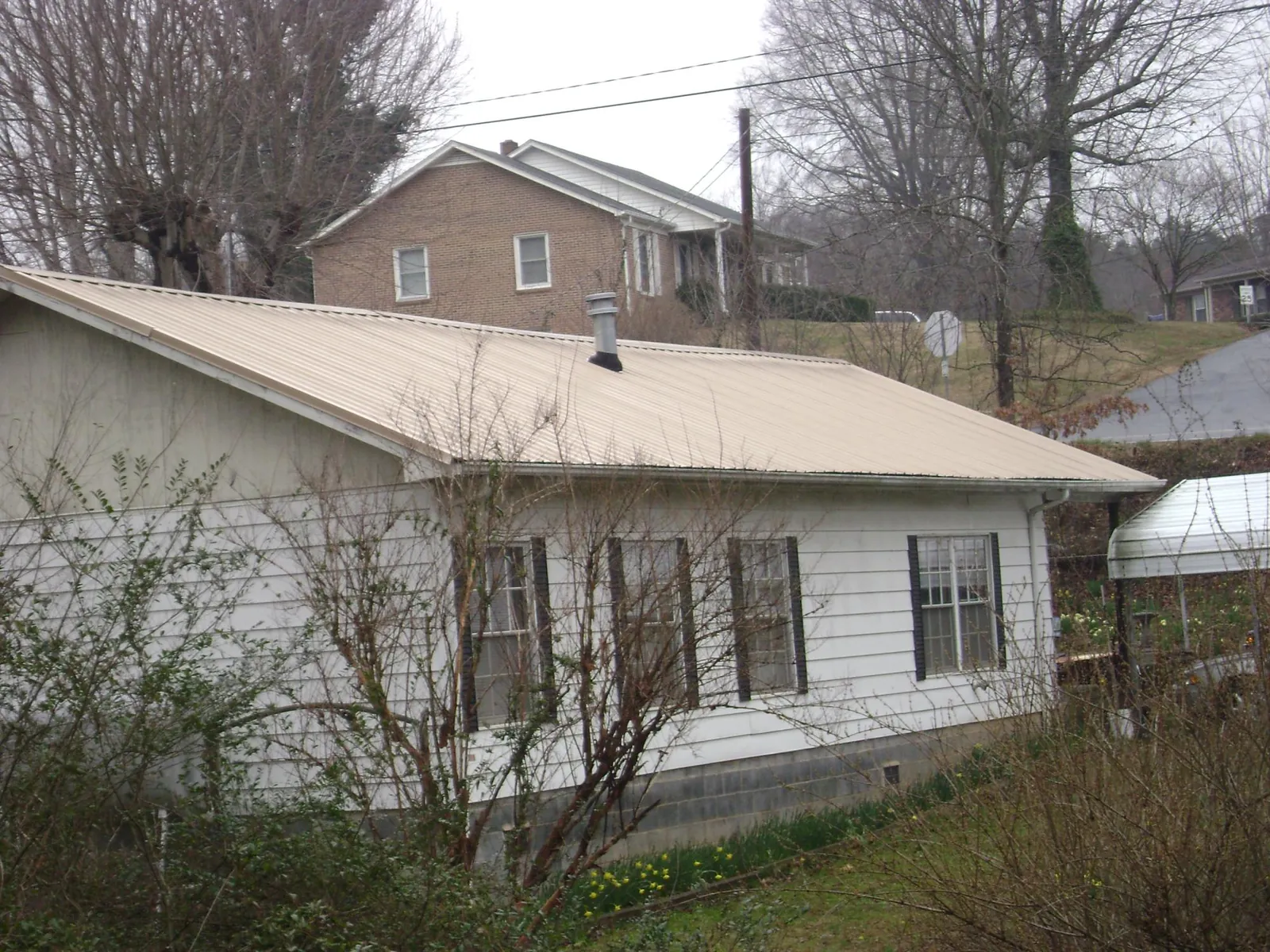 Tan metal roof on a white sided house set into a hillside — Commercial Roofing by Roofing Brothers in Westville